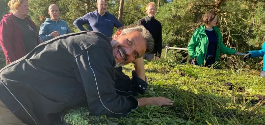 Rolando stützt sich auf ein Gründach und lächelt in die Kamera. Im Hintergrund steht die Seminargruppe, die bei der Begrünung des Dachs geholfen hat.