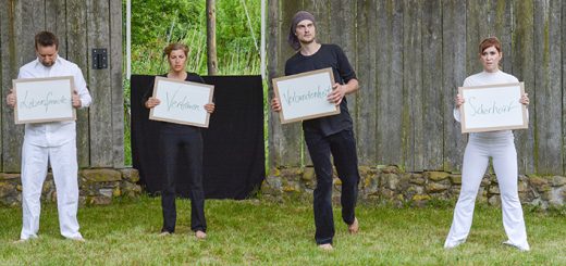4 Menschen stehen auf einer Bühne und halten ein jeweils ein Schild in der Hand