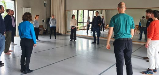 Eine Gruppe steht im Kreis in einem Raum und macht eine Übung